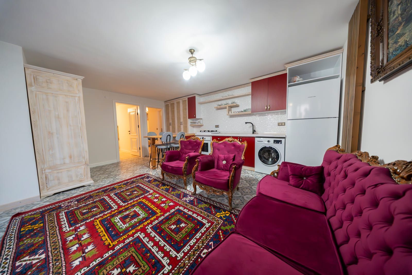 Dairenin oturma alanı; kilim, kadife koltuklar ve açık mutfak